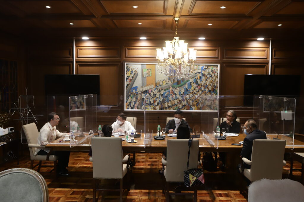 Alan Peter Cayetano attends a formal meeting with masked colleagues, separated by dividers, discussing policy, and engaging in governance safely.