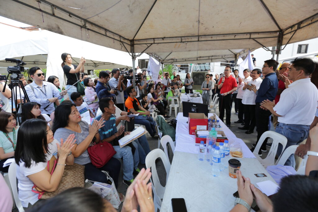 Alan Peter Cayetano addresses a crowd at an outdoor event, receiving applause and media attention during a public appearance.