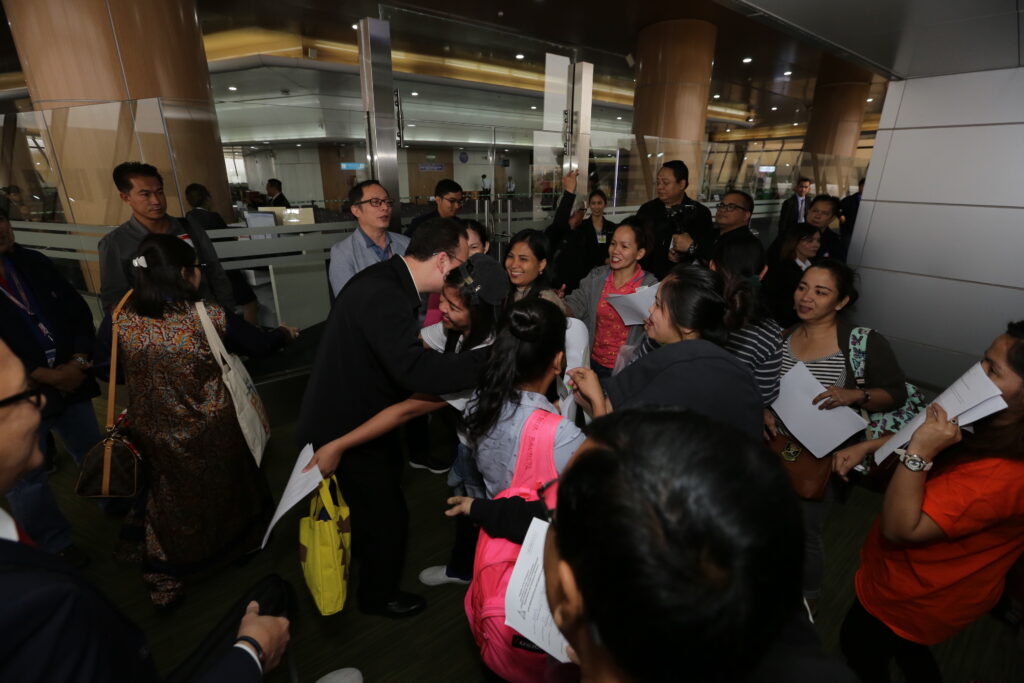 Alan Peter Cayetano is greeted warmly by a crowd, possibly overseas workers, at an airport arrival, showing support.