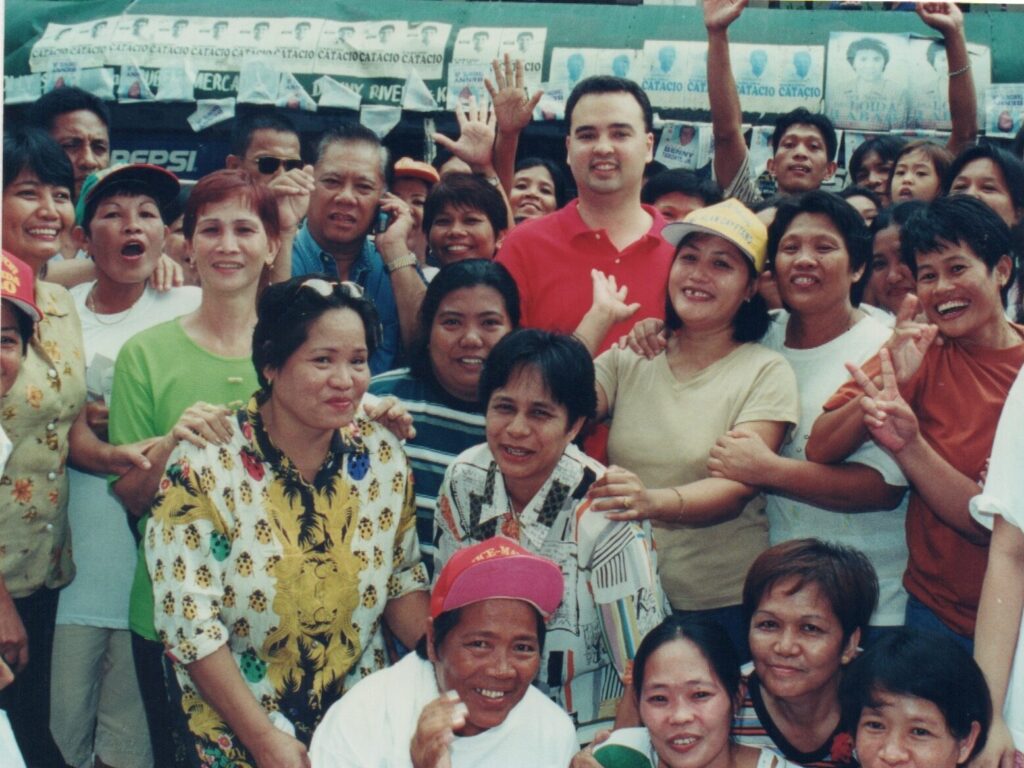 Alan Peter Cayetano poses with a crowd of supporters, likely during a political campaign or community event, showing public engagement.