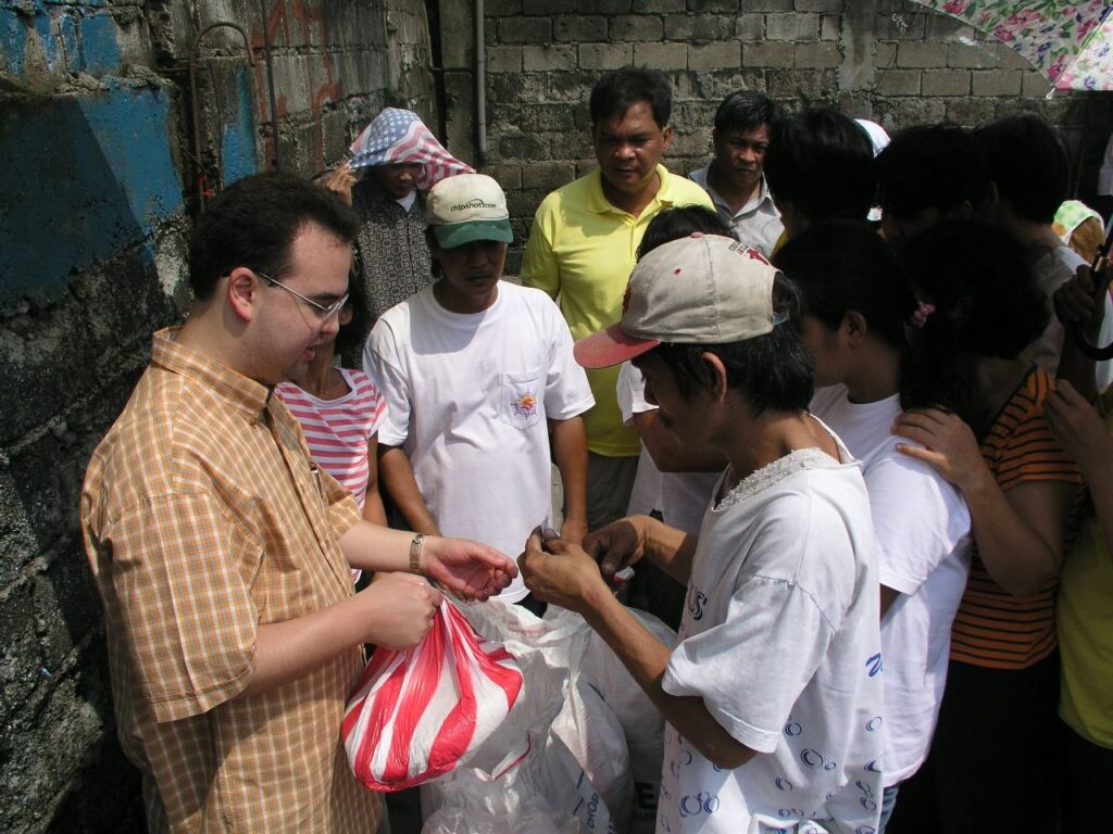 Alan Peter Cayetano distributes aid to a crowd, showing support, engaging directly, and providing assistance to those in need in a community.